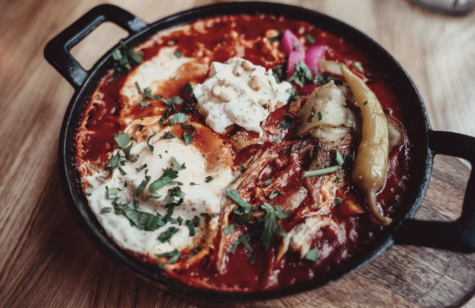 A shakshuka in a cast-iron pan — eggs set in a red pepper and tomato sauce, scattered with coriander